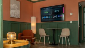 A hotel room with a large flat-screen TV displaying streaming services, a round wooden table, two chairs, a sofa, and a wall-mounted lamp. - Condo On The Beach - Heated Pool - Self Check-in (Belleair Beach)