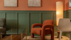 A room with a green wainscoting, two orange chairs, a white chair, a glass table, and a floor lamp. - Condo On The Beach - Heated Pool - Self Check-in (Belleair Beach)