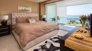 A bedroom with a large bed, a ceiling fan, a nightstand, a desk with a vase of flowers, and a view of the ocean through a sliding glass door. - Modern- Renovated- Breathtaking 6th Floor- 3 Bedrooms Villa Magna (Nuevo Vallarta)