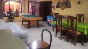 A room with a pool table, a dining table with chairs, a sofa, and a small table with a chair.