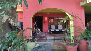 A pink building with a covered entrance, a table with chairs, and several potted plants. - Apart-Hotel Costa Verde Distrito Nacional (Santo Domingo Oeste)