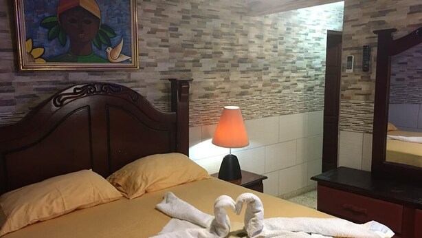 A hotel room with a bed, a nightstand with a lamp, a painting on the wall, and a mirror.