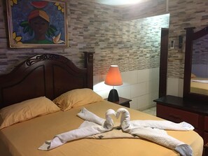 A hotel room with a bed, a nightstand with a lamp, a painting on the wall, and a mirror. - Apart-Hotel Costa Verde Distrito Nacional (Santo Domingo Oeste)