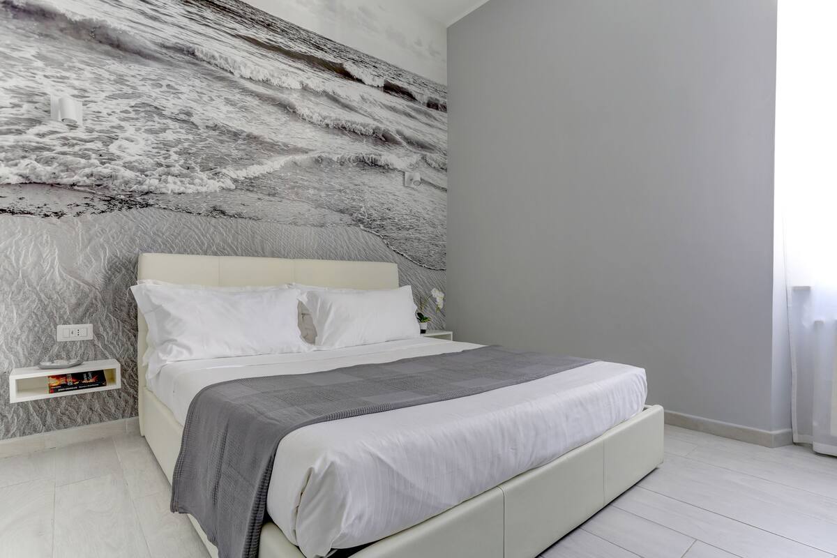 A modern bedroom with a bed, a nightstand, and a wall-mounted shelf.