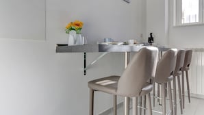 A modern kitchen with a dining area, featuring a bar counter, chairs, and a vase with flowers. - Voyager House (Rome)