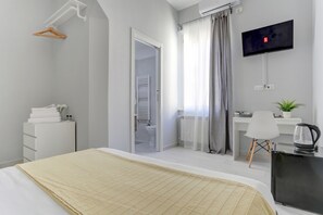 Habitación de hotel moderna con cama, escritorio, televisor y baño visible a través de una puerta abierta.