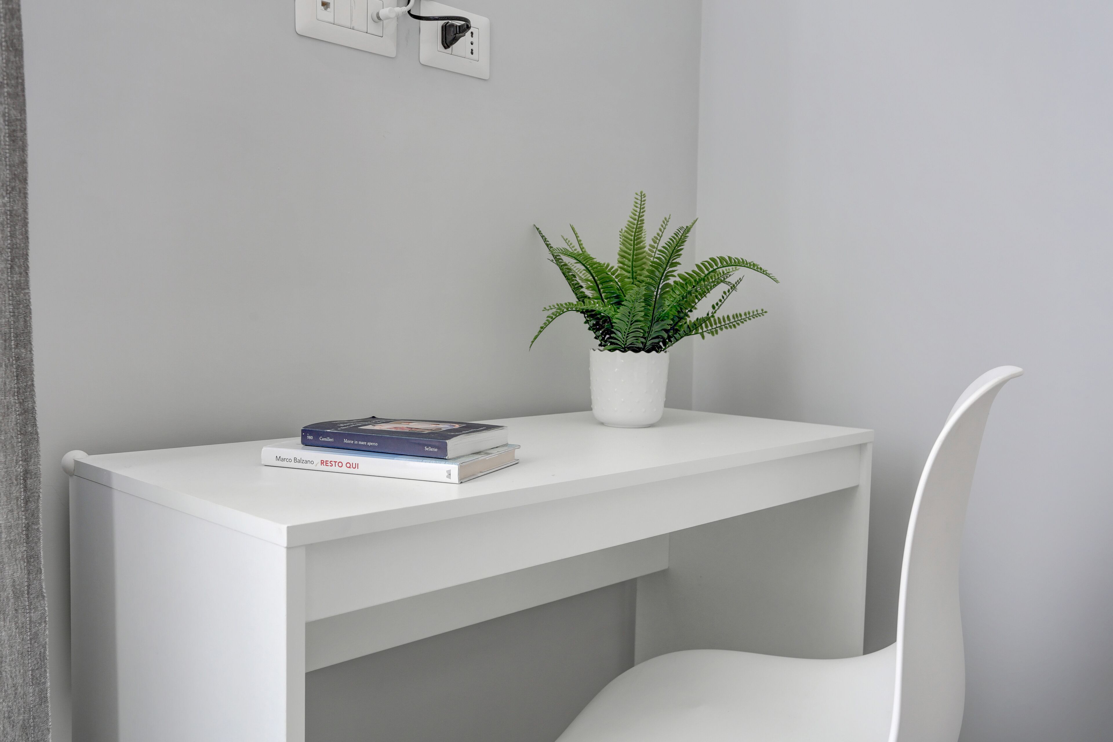 Een wit bureau met een potplant en een boek getiteld 'Marco Balzano - RESTO QUI'.
