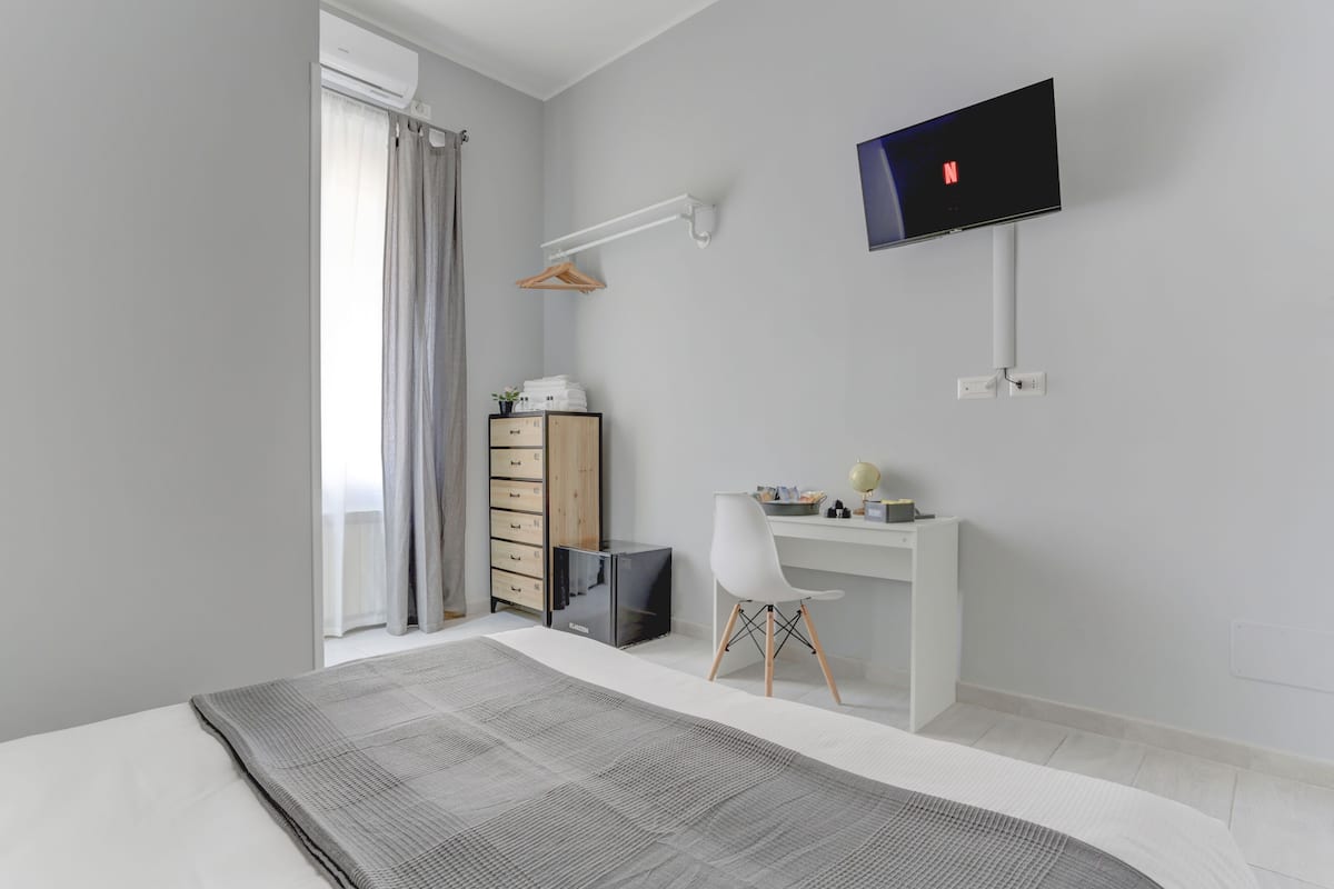 A modern bedroom with a bed, a desk, a chair, a TV, and a wardrobe.
