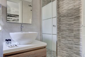 Un baño moderno con un lavamanos grande de color blanco, un espejo y una cabina de ducha de vidrio.
