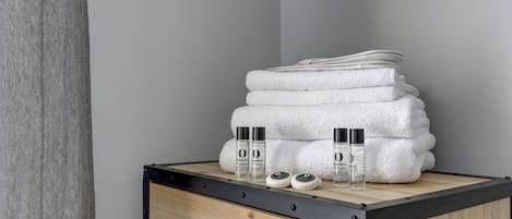 A wooden bedside table with a stack of white towels and two bottles of lotion.