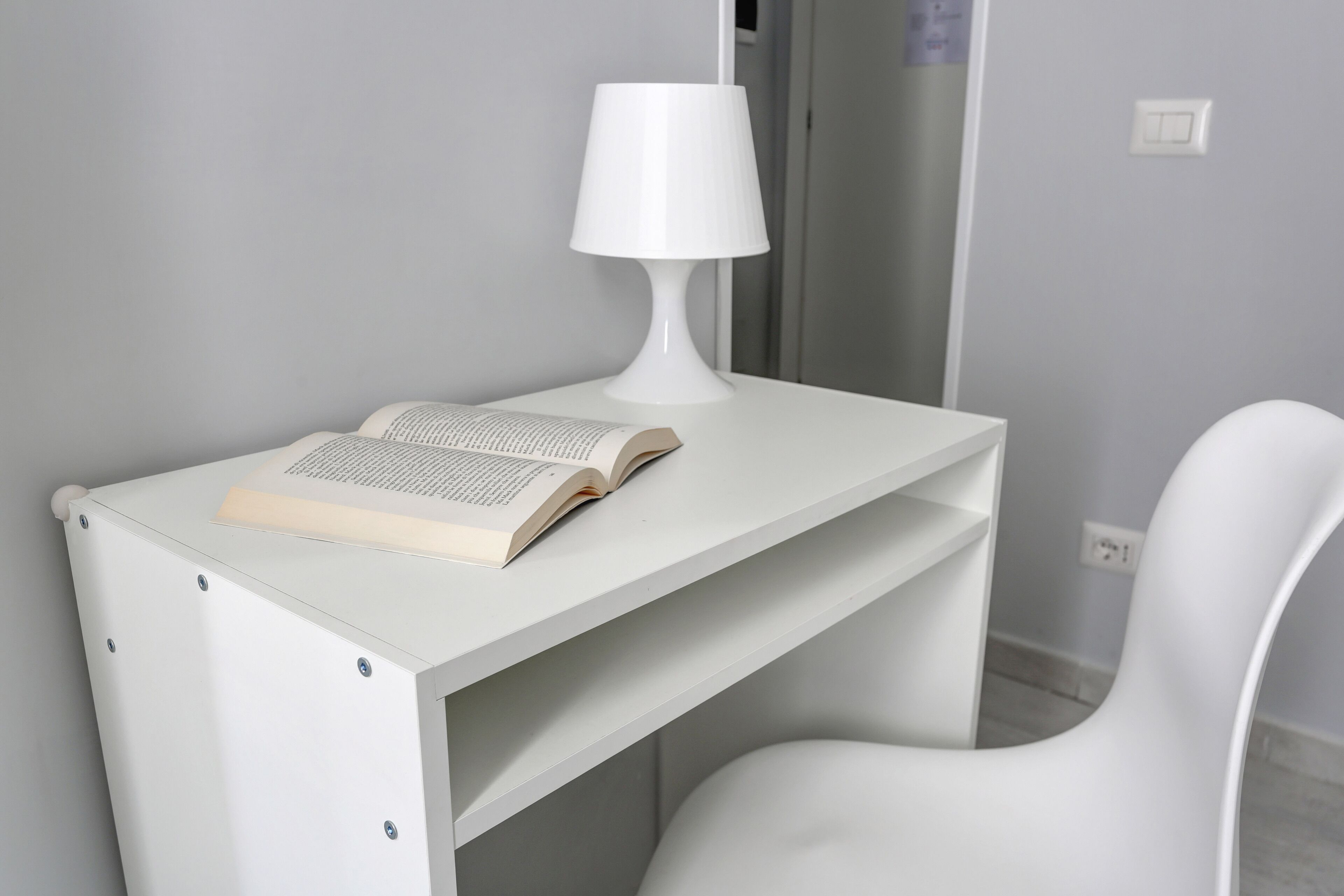 A white desk with a lamp and an open book.
