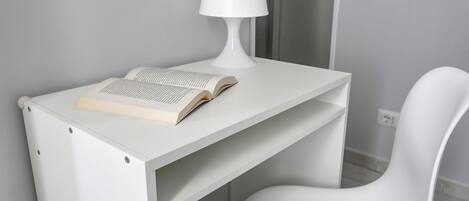 A white desk with a lamp and an open book.
