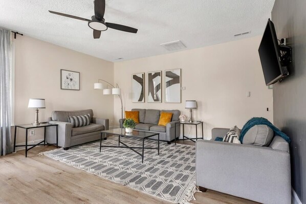 A modern living room with a grey sofa, a coffee table, and a TV mounted on the wall.