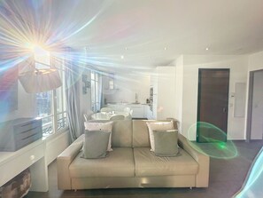A modern living room with a sofa, a dining table, and a kitchen in the background. - Premium Design Renovated 2 BR 2 bath Croisette 200 m Olam Properties (Cannes)