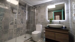 Un baño con baldosas estampadas, un inodoro, un lavamanos con espejo y una cabina de ducha.