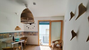 Una habitación con una mesa de comedor, sillas, una lámpara colgante, un reloj de pared y un ventanal corredero que da a un balcón.