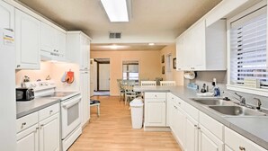 Una cocina moderna con armarios blancos, horno integrado, un lavabo y una zona de comedor con mesa y sillas.