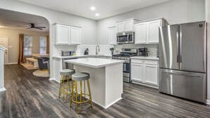 A modern kitchen with white cabinets, stainless steel appliances, and a central island with stools. - Stylish 8-Guest Getaway with Fire Pit & Modern Comforts (Spring)