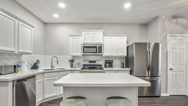 A modern kitchen with white cabinetry, stainless steel appliances, and a central island with stools. - Stylish 8-Guest Getaway with Fire Pit & Modern Comforts (Spring)