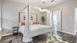 A bedroom with a four-poster bed, a ceiling fan, a nightstand, a plant, and a rug. - Stylish 8-Guest Getaway with Fire Pit & Modern Comforts (Spring)