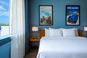 A hotel room with a large bed, two wall-mounted lamps, and two posters on the wall.