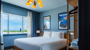 Habitación de hotel con una cama grande, vistas al mar y una estantería de madera con toallas.