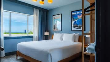 A hotel room with a large bed, a view of the sea, and a wooden shelf with towels.