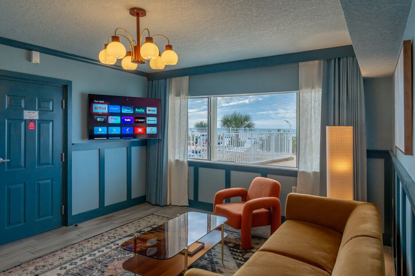 Habitación de hotel con una televisión mostrando servicios de streaming, un sofá, una mesa de centro y vistas al exterior.