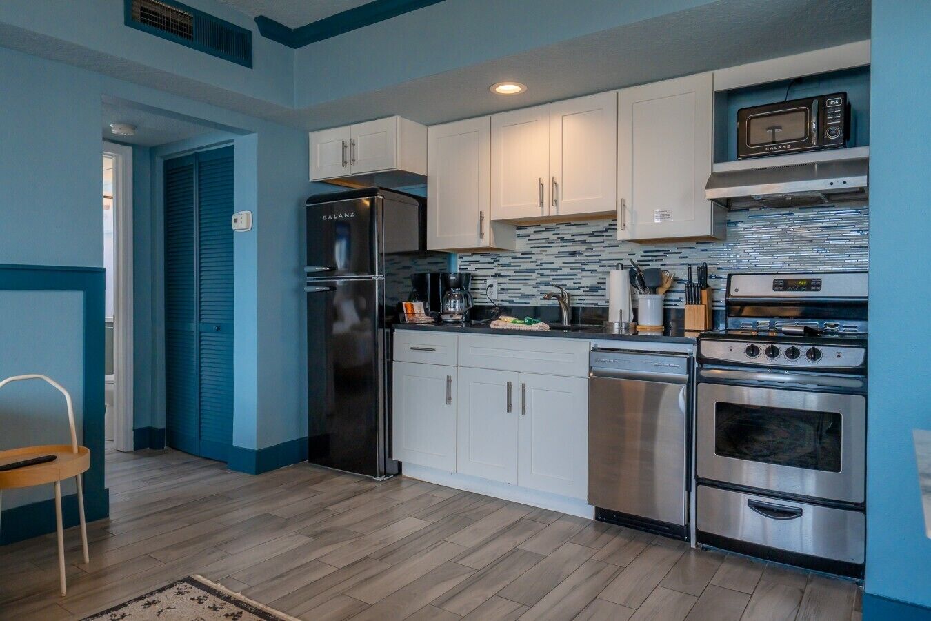Una cocina compacta con gabinetes blancos, un refrigerador de acero inoxidable, un lavavajillas y una estufa.