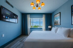 A hotel room with a large bed, a flat-screen TV displaying streaming services, a window with curtains, and a cityscape view.