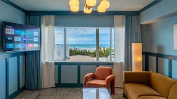 A hotel room with a large window, a flat-screen TV displaying streaming services, a sofa, a chair, and a patterned rug.