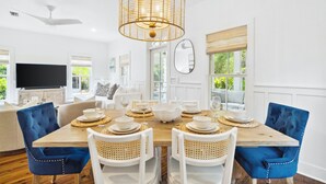 A dining room with a wooden table set for six, white chairs, and a large chandelier.