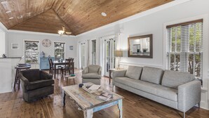 A spacious living area with a wooden ceiling, a grey sofa, a coffee table, and a dining area with chairs and a table.
