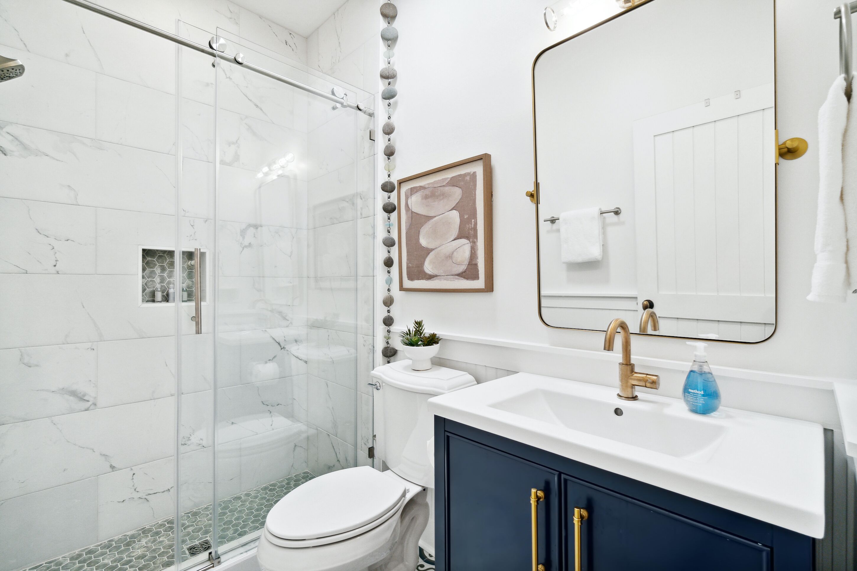 Un baño moderno con cabina de ducha de vidrio, inodoro blanco, lavamanos con grifo dorado y mueble oscuro azul.