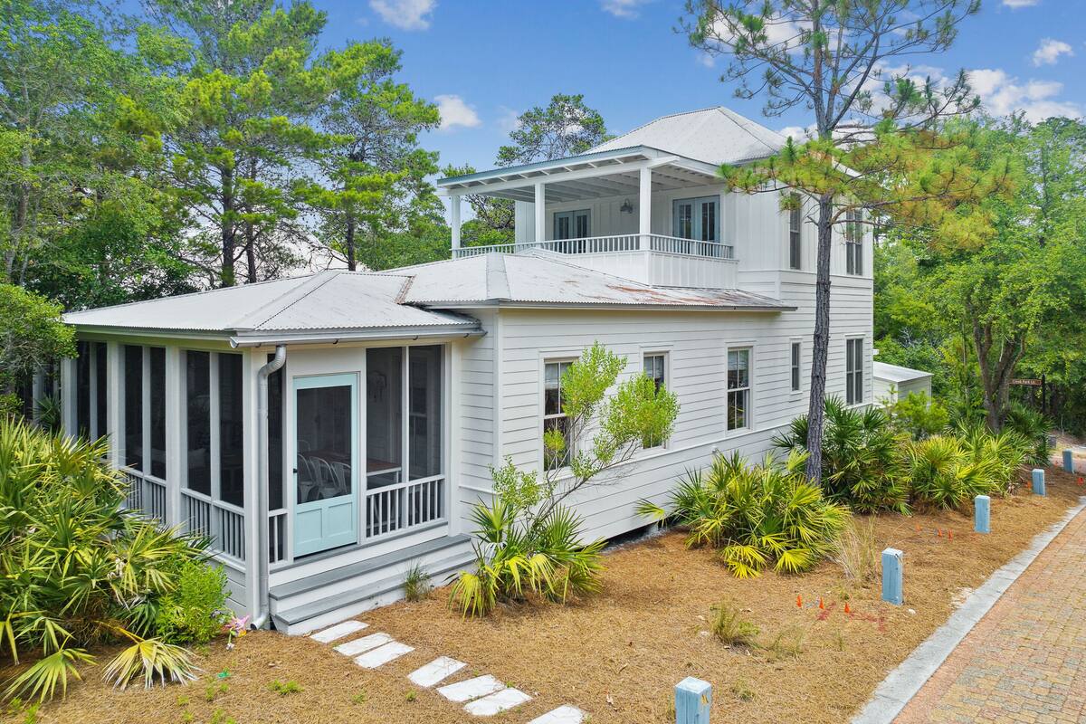 A two-story house with a porch, surrounded by trees and plants.