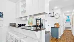 A modern kitchen with white cabinetry, a central island with bar stools, a clock, and artwork on the walls.