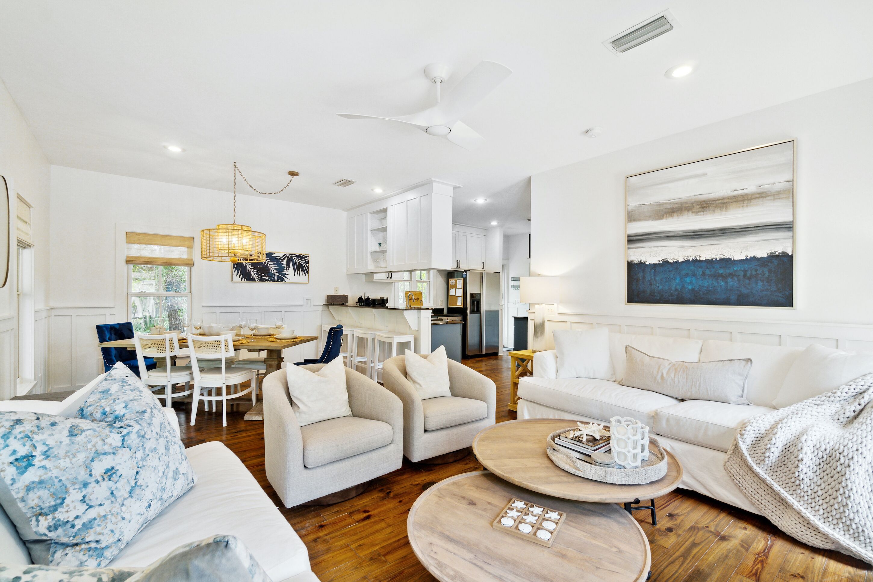 A spacious living room with a white sofa, two armchairs, a coffee table, and a dining area with a white table and chairs.