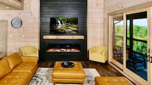Una sala de estar acogedora con chimenea, televisor montado encima y un ventanal con vistas al exterior.