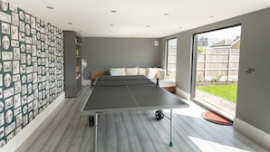 A room with a ping pong table, a sofa, and a wall covered with pictures. - Sunbeam and Sundance Cosy House (whitstable)
