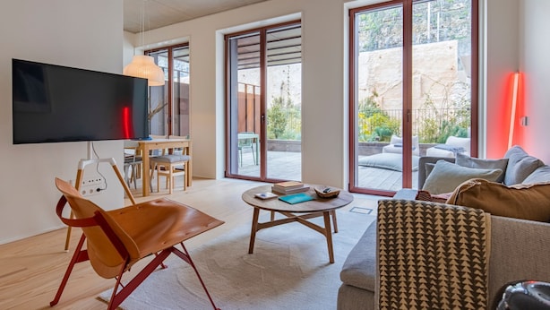 Ein modernes Wohnzimmer mit Flachbildfernseher, Essbereich mit Tisch und Stühlen, einer Couch und großen Schiebeglasüren zum Außenbereich.