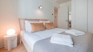 Ein ordentlich bezogenes Bett mit Kissen und einem gefalteten Handtuch, eine Nachttischlampe und ein Kleiderschrank in einem Hotelzimmer.