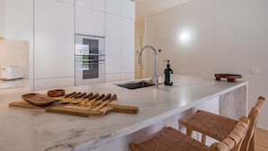 Eine moderne Küche mit weißen Schränken, einem eingebauten Backofen, einer Edelstahl-Spüle und einer Marmorarbeitsplatte.