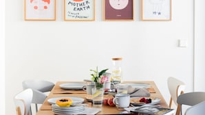 Ein Esstisch ist gedeckt mit Tellern, Besteck, einer Karaffe, einer Blumenvase und verschiedenen Speisen.