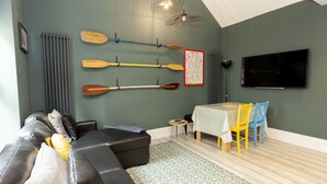 A living room with a sofa, a table with chairs, a TV, and wall-mounted paddles. - Sundance Cosy Getaway (whitstable)