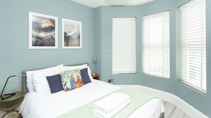 A bedroom with a bed, two wall-mounted artworks, a bedside table, and a window with blinds. - Sundance Cosy Getaway (whitstable)