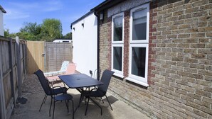 A patio with a table and chairs, a brick wall, and a wooden fence. - Sundance Cosy Getaway (whitstable)