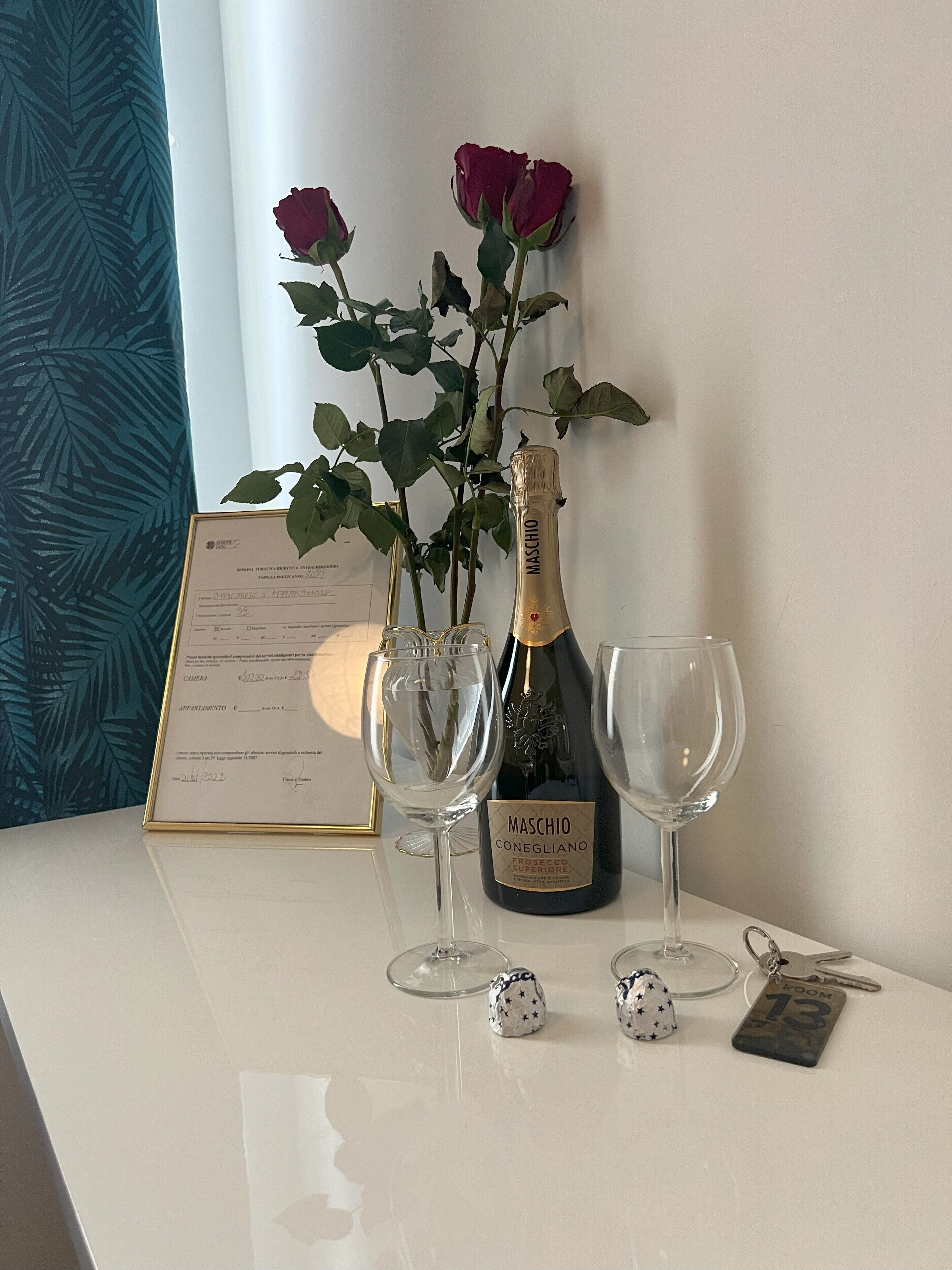 Ein Tisch mit einer Flasche Maschio Conegliano Prosecco, zwei Weingläsern, einer gerahmten Speisekarte und einem Schlüsselanhänger mit einer Zimmernummer.