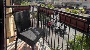 A balcony with a wicker chair, potted plants, and a view of a street with buildings and a hill in the background. - Suitedream Vatican (Rome)