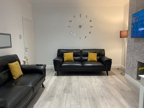 Relax in this stylish living room with a black leather sofa, flat-screen TV, and floor lamp.