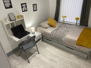Relax in a serene space with a neatly made bed, a desk for work, and a comfortable chair.